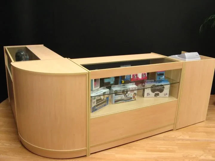 Curved wooden Cosmos Counter Set with a glass display top, showcasing various products inside, on a light wood floor
