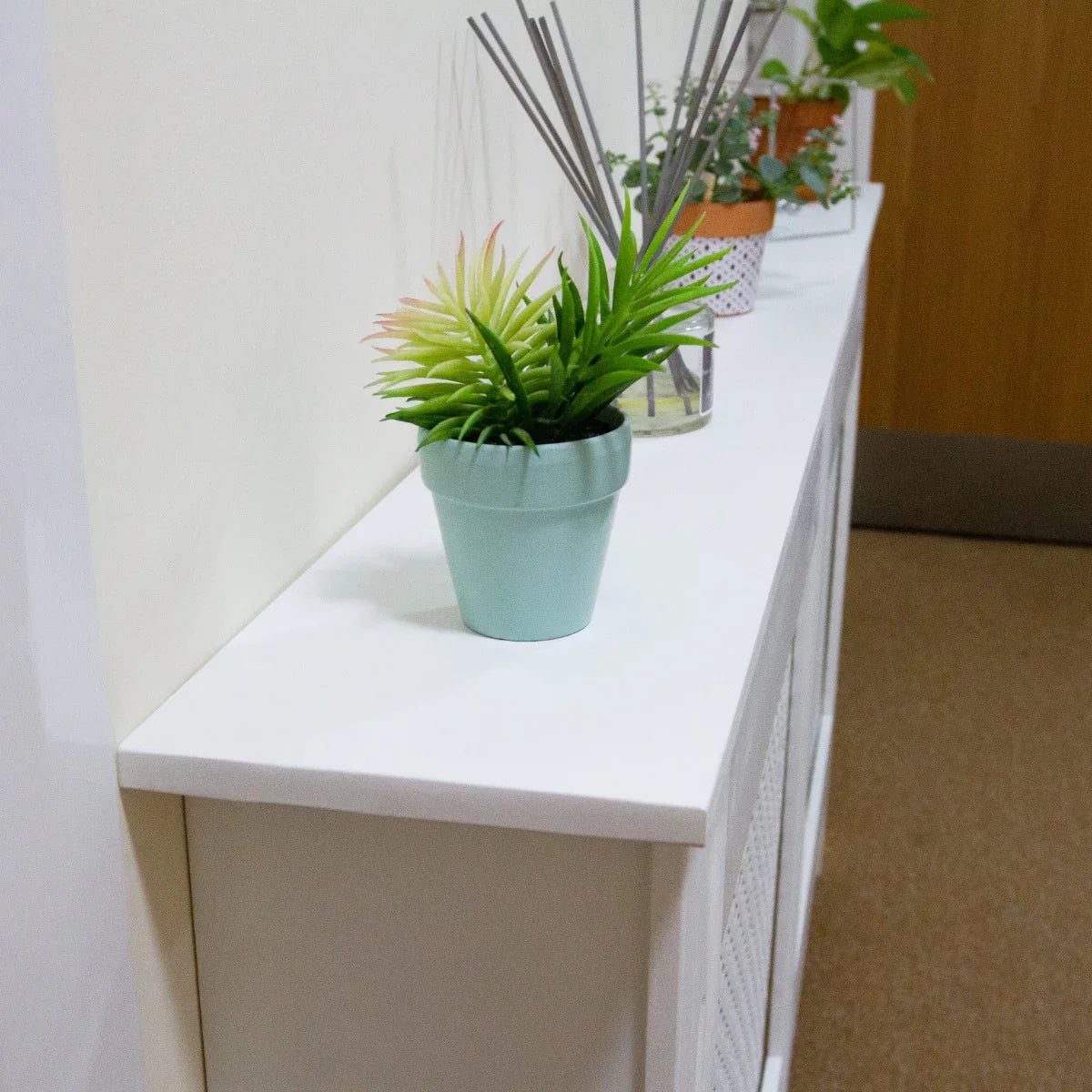 Unfinished MDF radiator cover with a smooth white top, featuring a light blue plant pot and decorative items on display