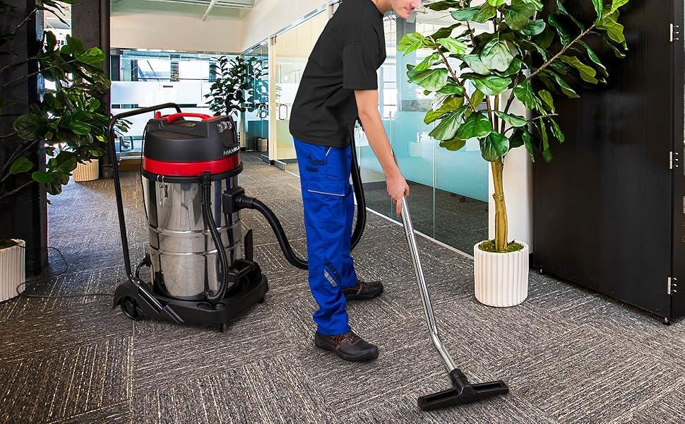 A person in blue work pants uses a silver and red vacuum cleaner on a textured gray carpet in a modern office setting