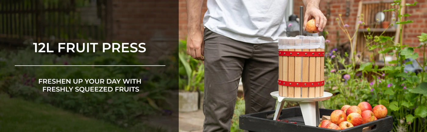 12L fruit press with wooden barrel design, metal base, and fresh apples nearby, ideal for making juice in a garden setting
