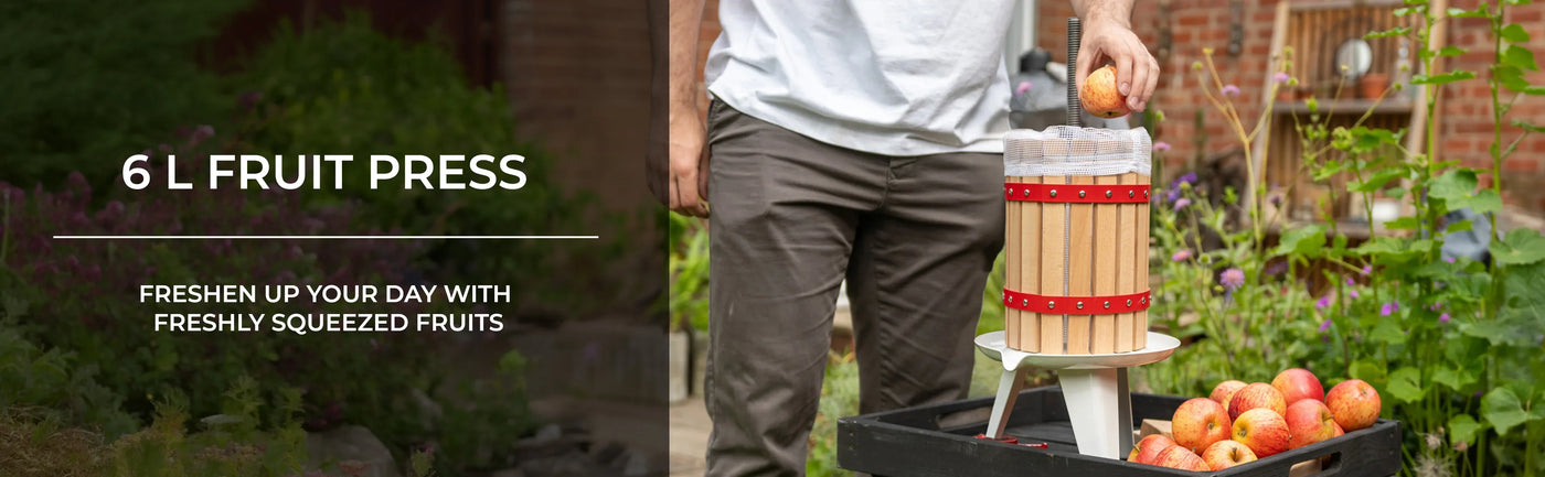 Wooden 6-liter fruit press with red accents, surrounded by fresh apples in a garden setting, ideal for making juice