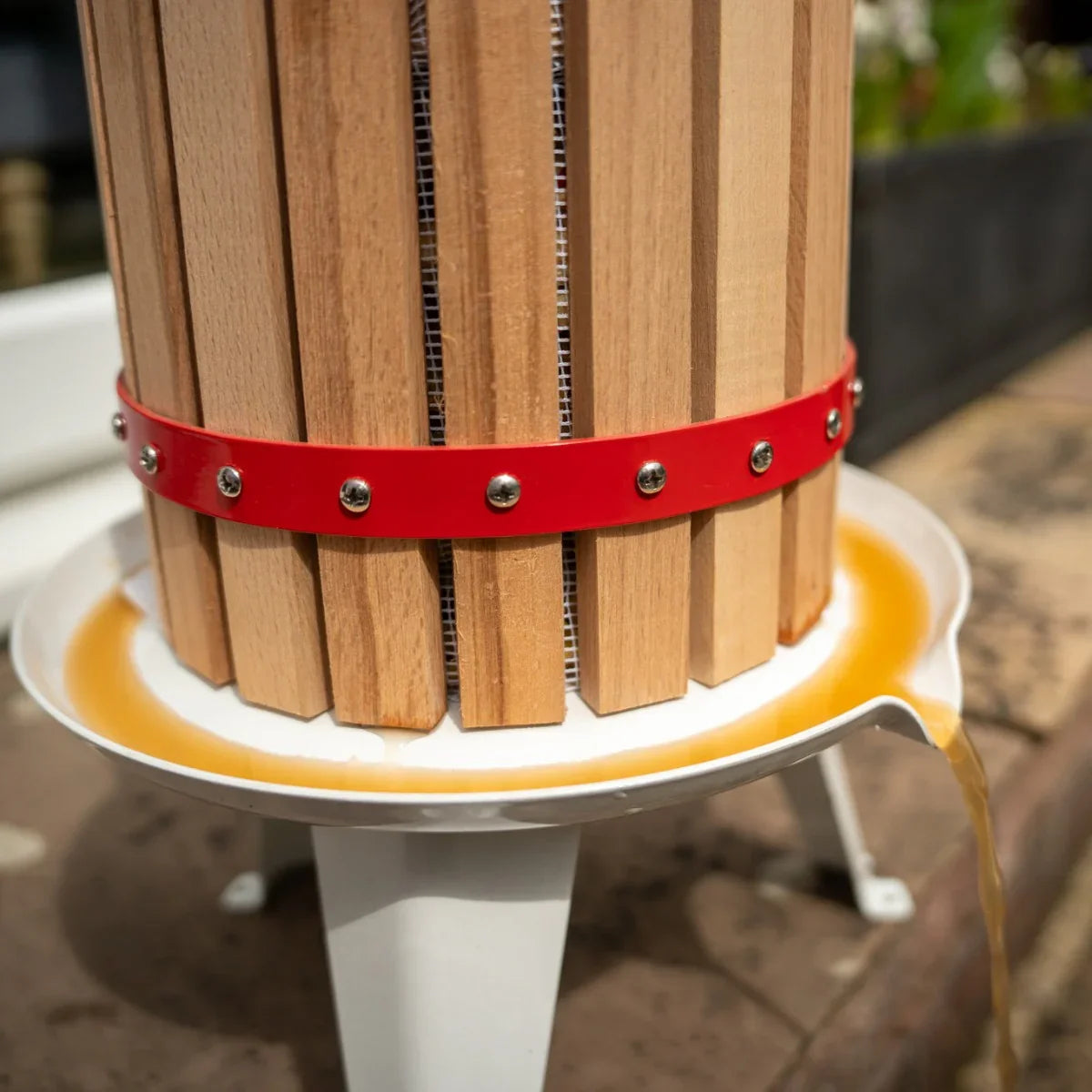 KuKoo 6 Litre Fruit Press with wooden slats, red metal band, and white base, showcasing fresh juice flowing from the spout