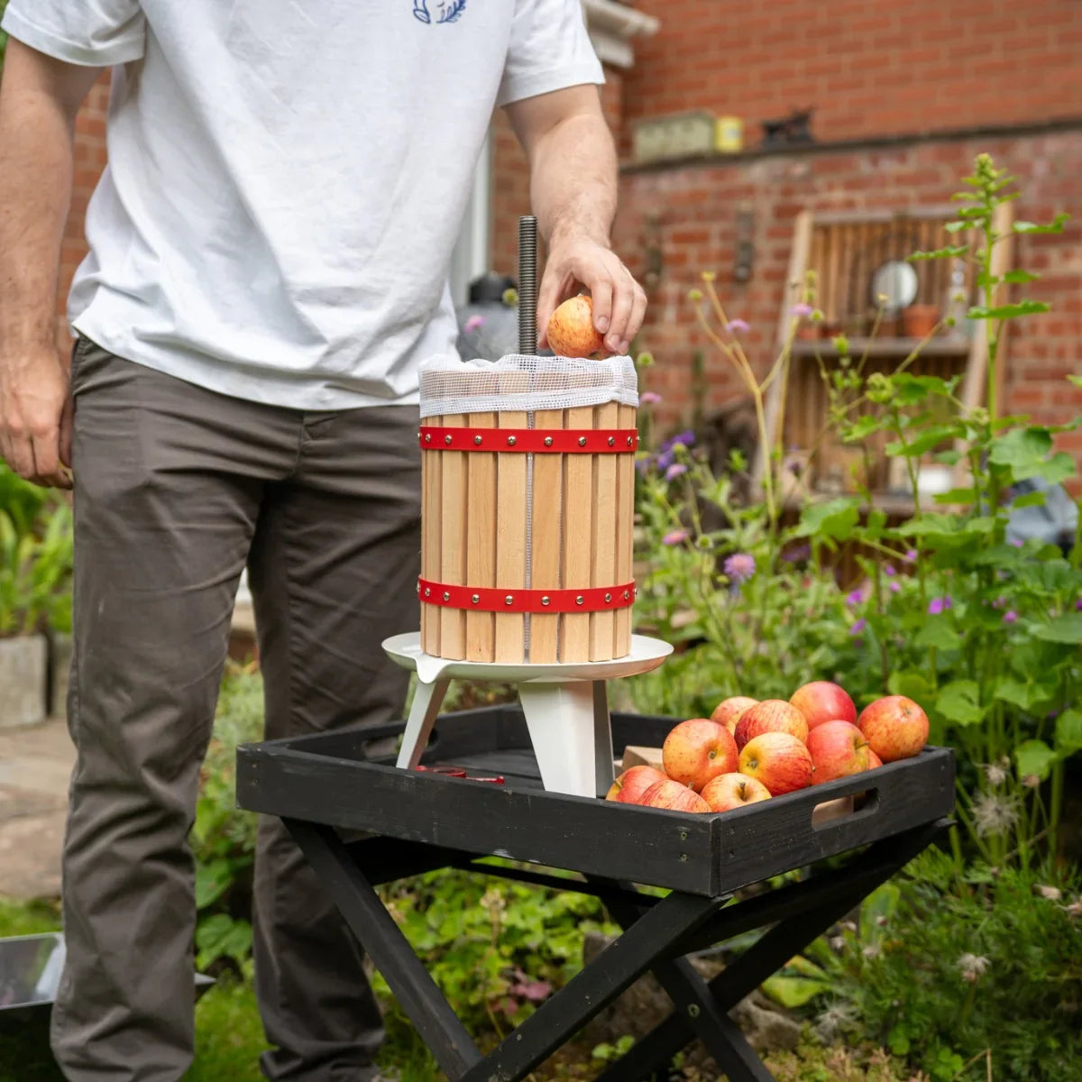 KuKoo 18 Litre Fruit Press with wooden slats and red accents, being used outdoors to press apples on a garden table