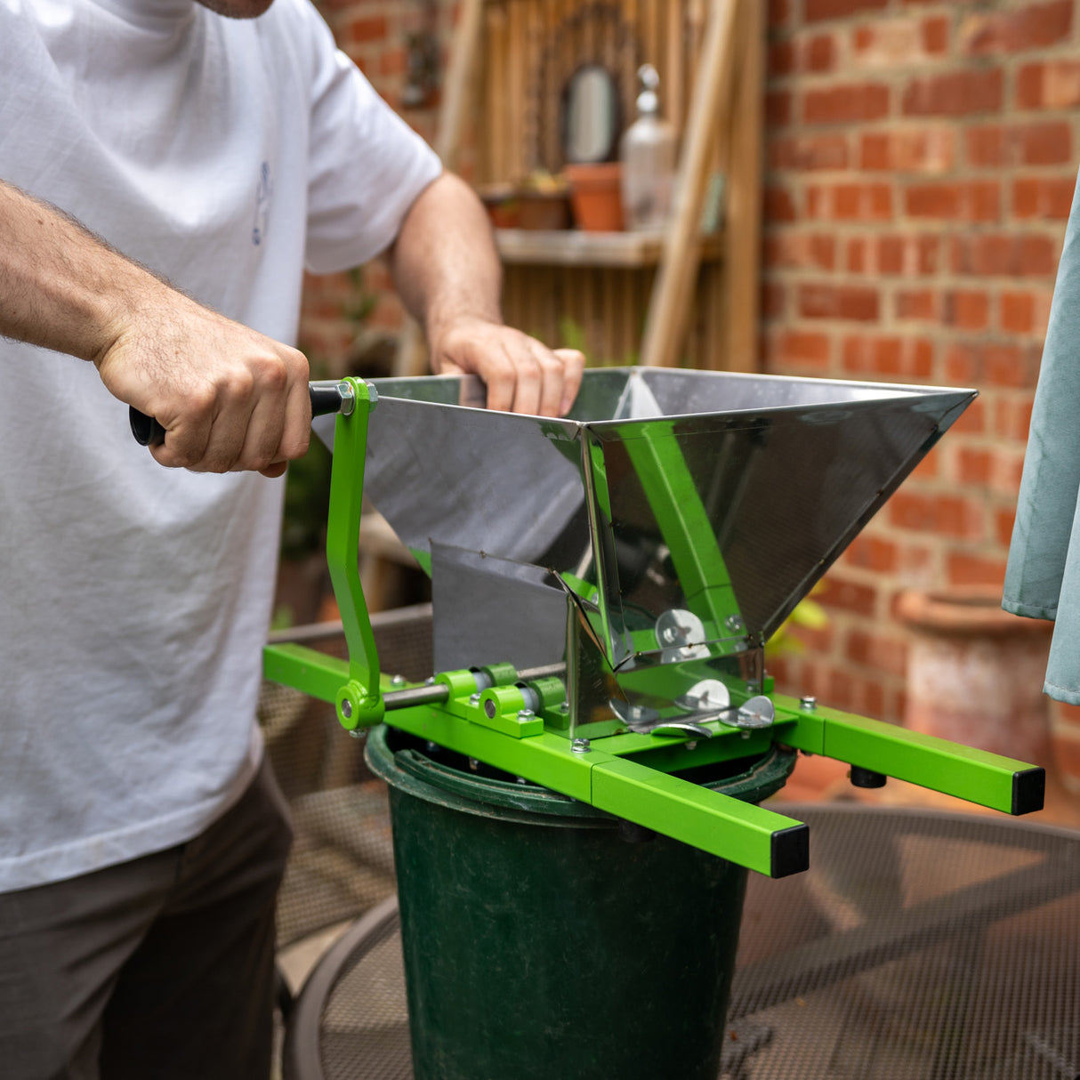 Green and silver 7-litre fruit crusher with a sturdy frame, being operated over a green bucket, ideal for juicing fruits