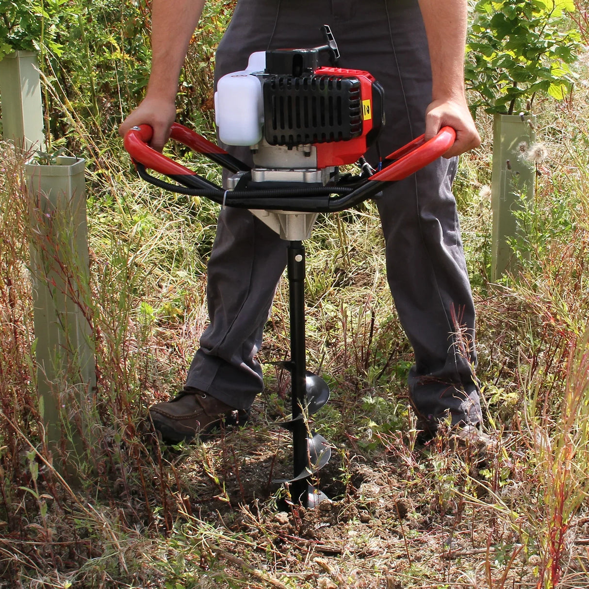Powerful Earth Auger with a 4-stroke engine, featuring red handles, digging into soil surrounded by tall grass and plants