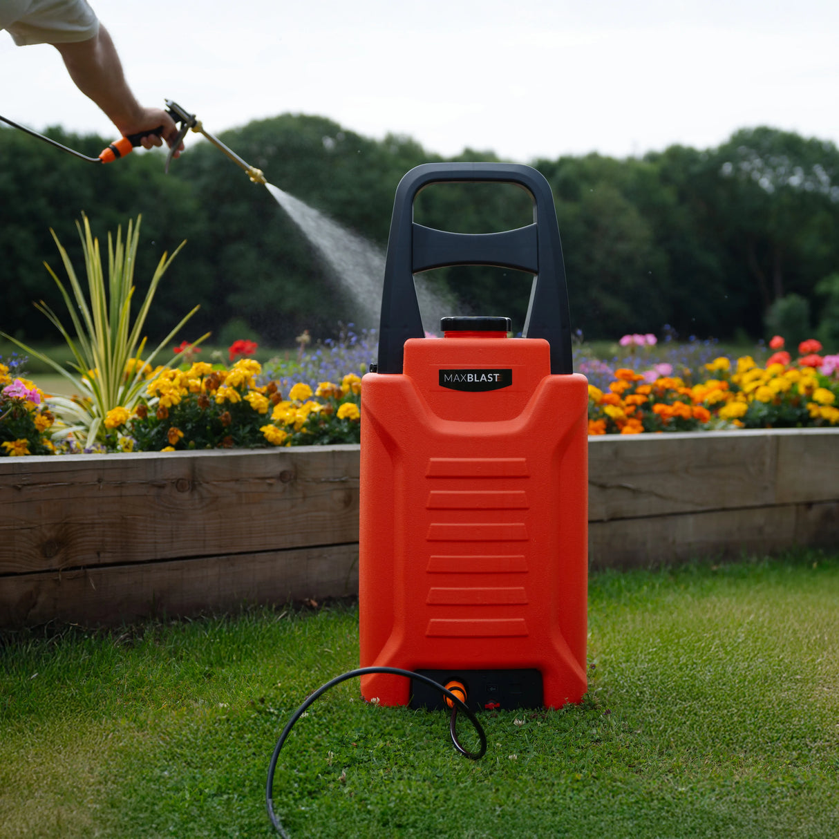 MAXBLAST 30L Cleaning Water Trolley in bright orange, featuring a sturdy handle and hose, set against a colorful flower garden
