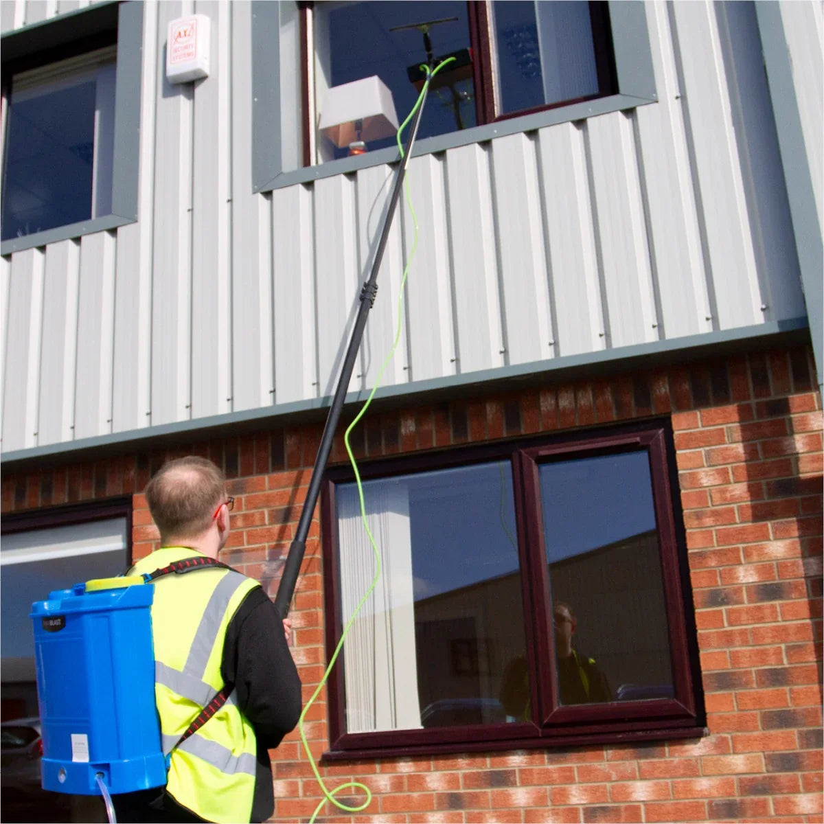 Water fed backpack with 16L capacity and 24ft cleaning pole, used for window cleaning on a commercial building exterior