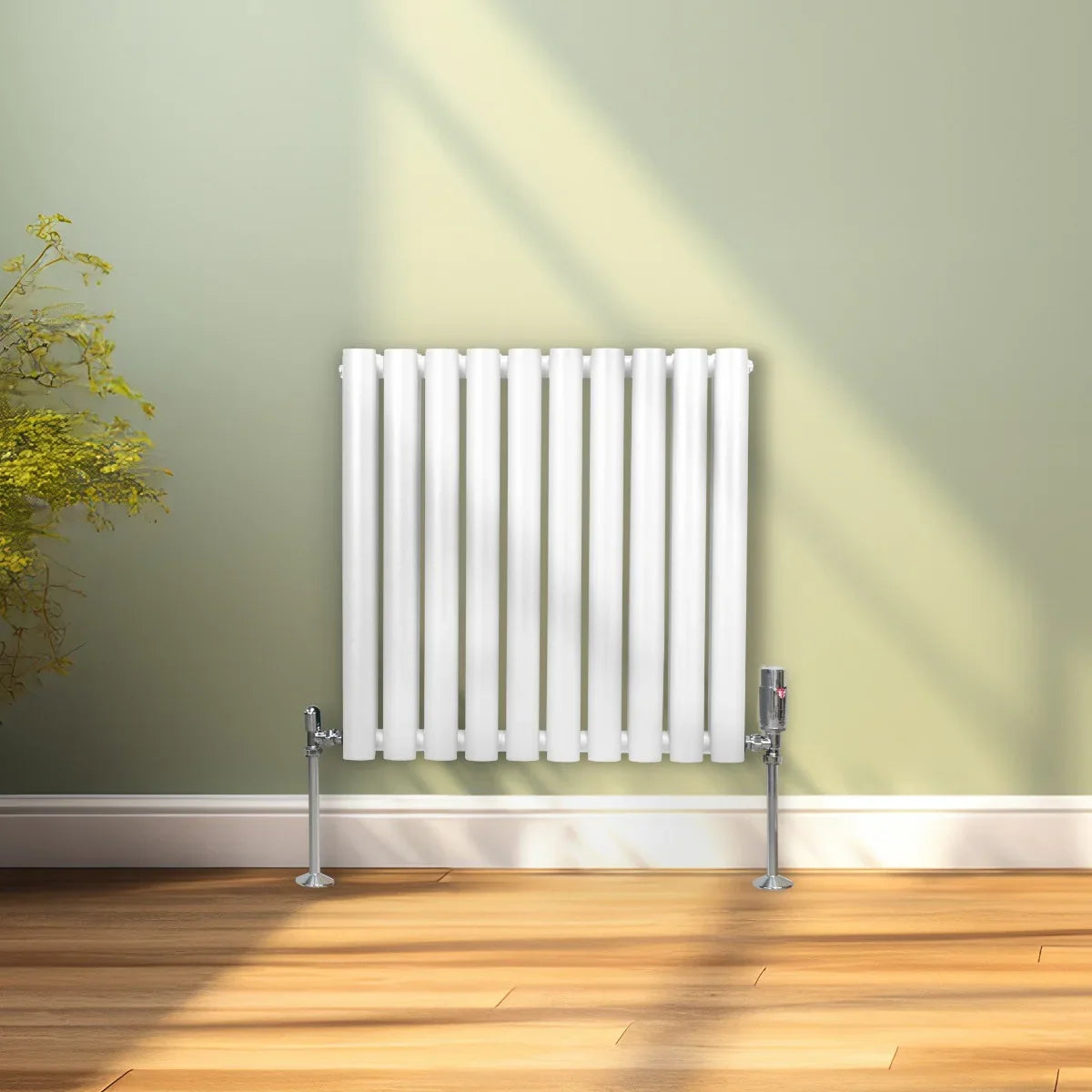 White oval column radiator with sleek vertical fins and chrome valves, mounted on a light wooden floor against a soft green wall