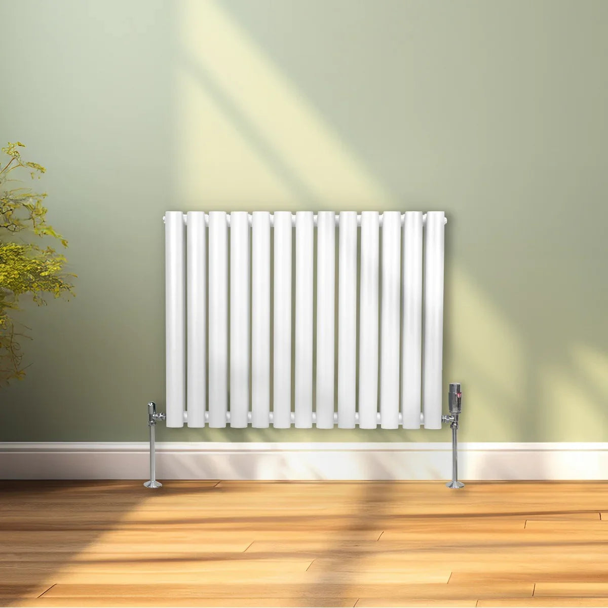Sleek white oval column radiator with vertical fins and chrome valves, set against a soft green wall and wooden floor