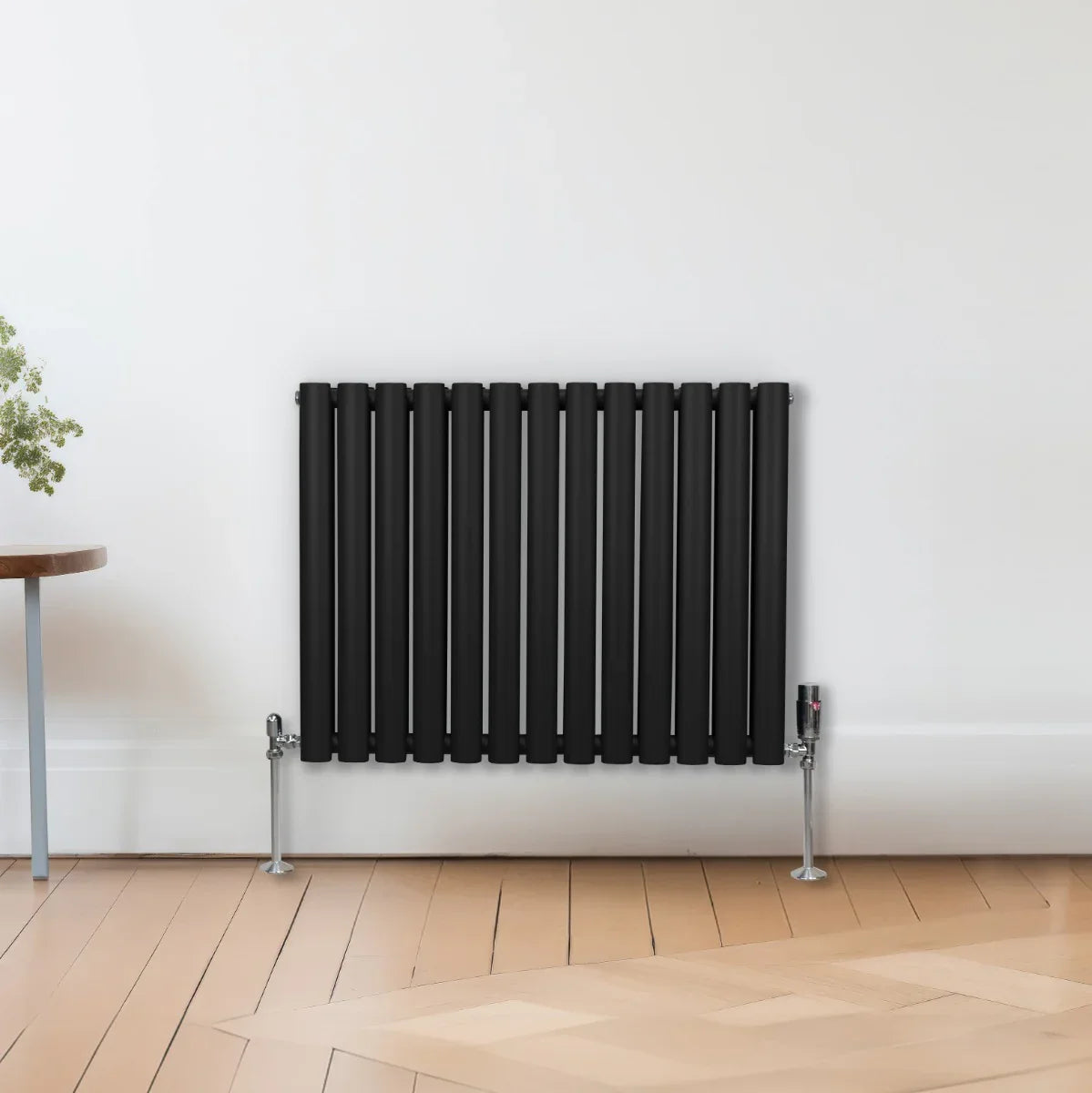Sleek black oval column radiator with vertical bars and valves, mounted on a light wooden floor against a white wall