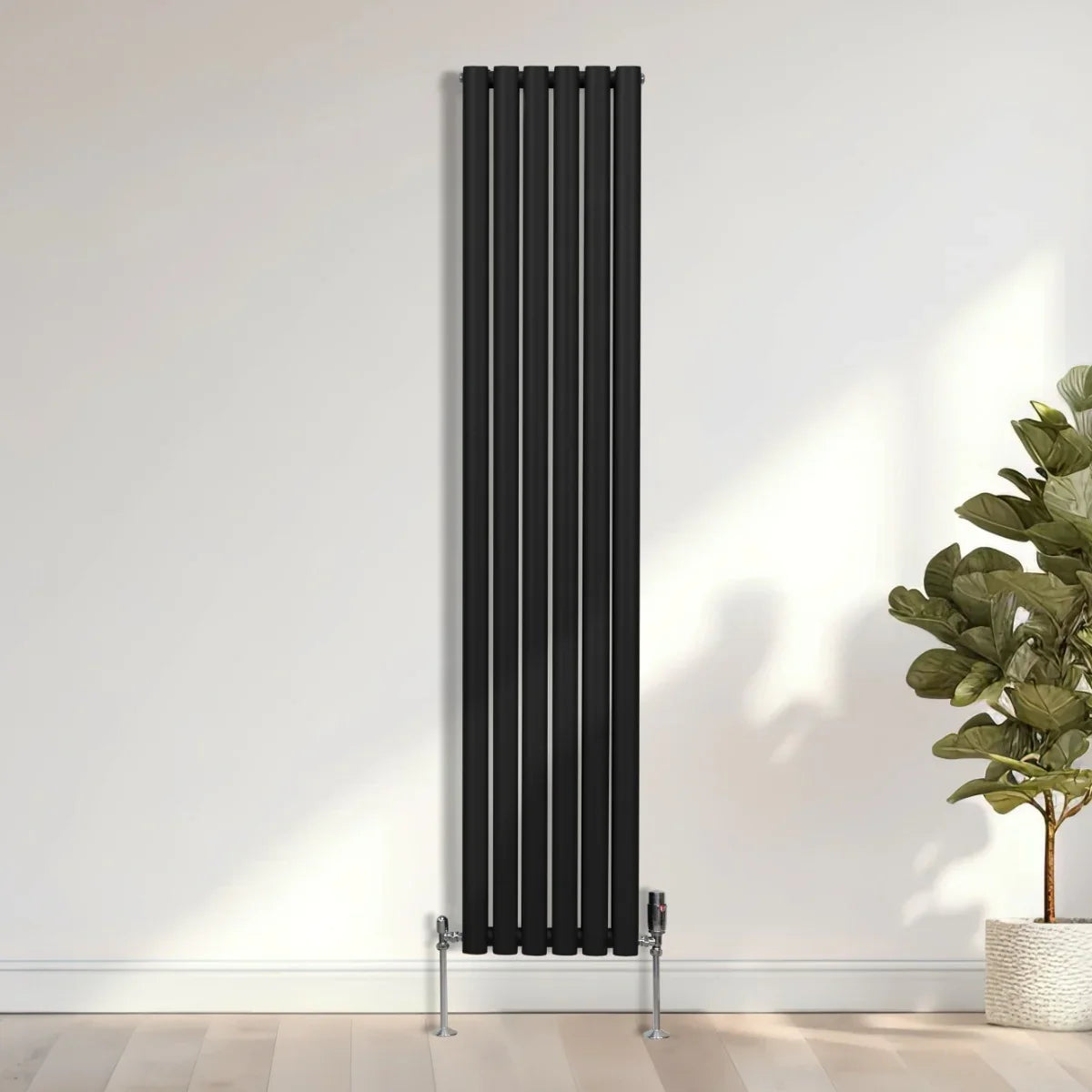 Sleek black oval column radiator, 1800mm x 360mm, featuring vertical bars and chrome valves, set against a light wall and plant backdrop