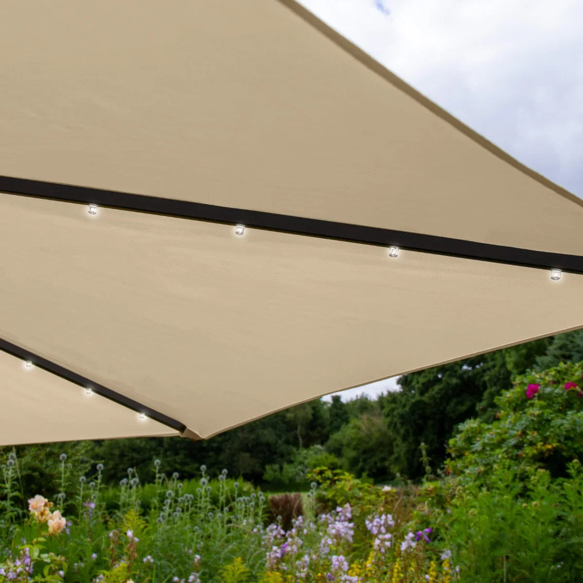 Beige 3m LED cantilever parasol with soft fabric canopy, illuminated edges, and sturdy black frame, set against a vibrant garden backdrop