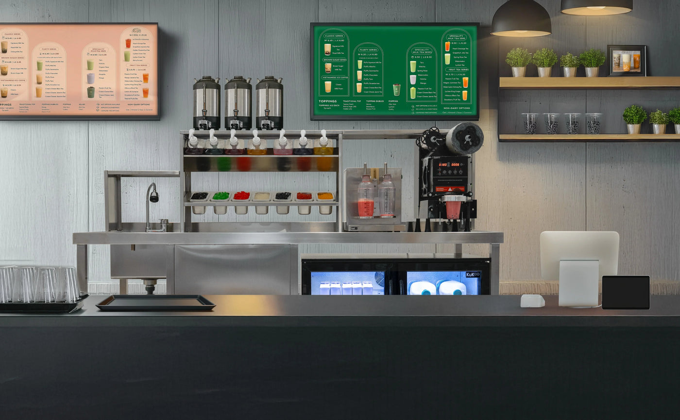 Modern beverage counter featuring colorful drink dispensers, menu boards, and sleek black surfaces, with green plants for decor