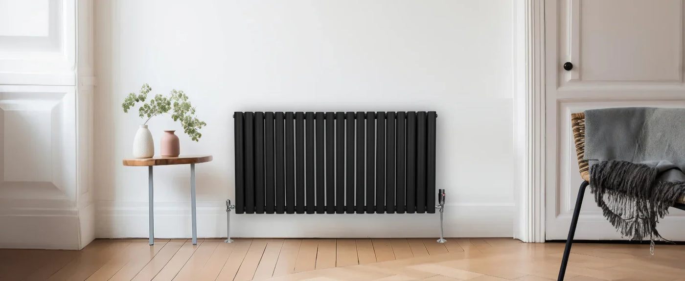 Sleek black radiator mounted on a white wall, accompanied by a wooden side table with a vase and greenery, in a modern room setting