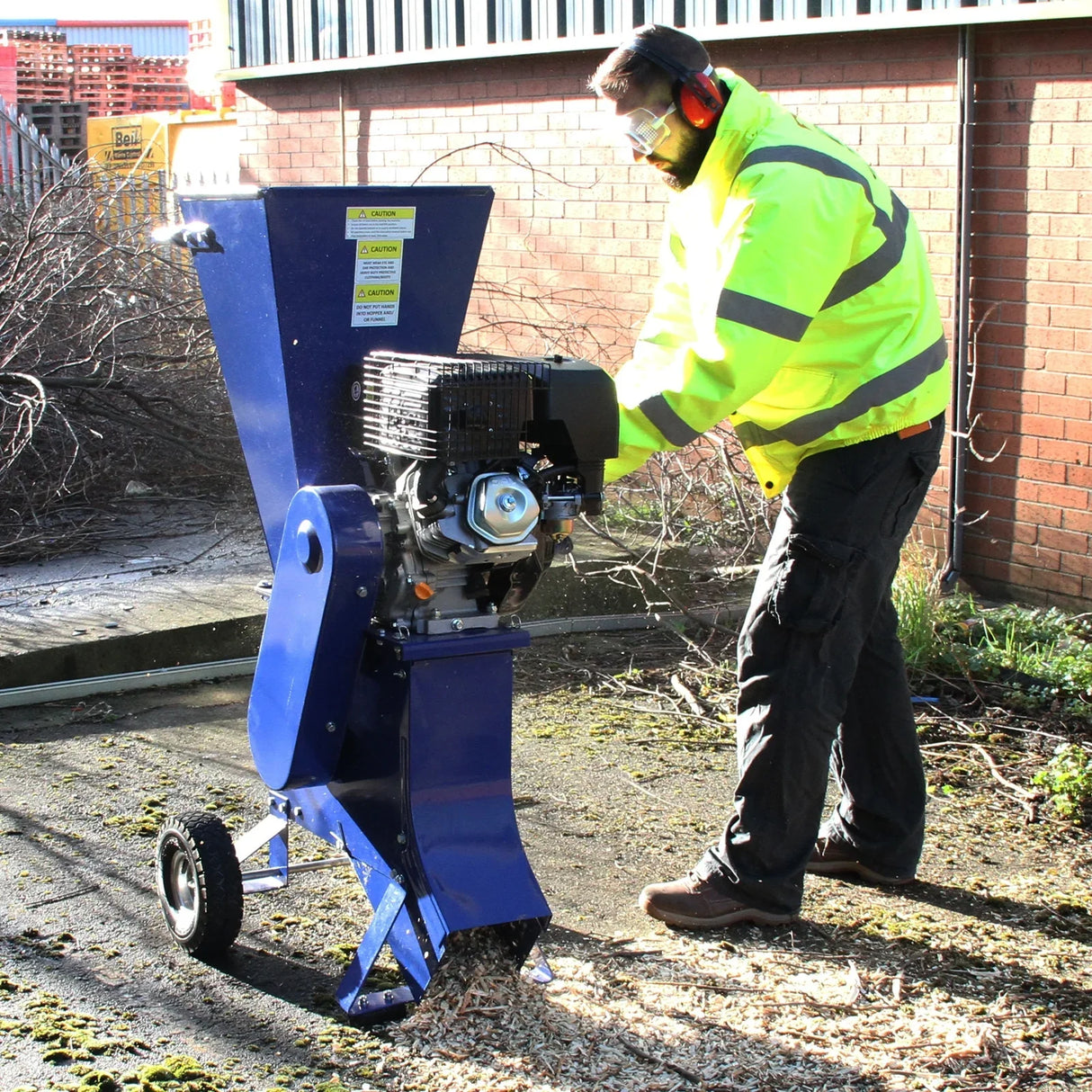 T-Mech 15HP wood chipper in blue, featuring a sturdy design, large chute, and a user wearing safety gear, processing branches on a sunny day