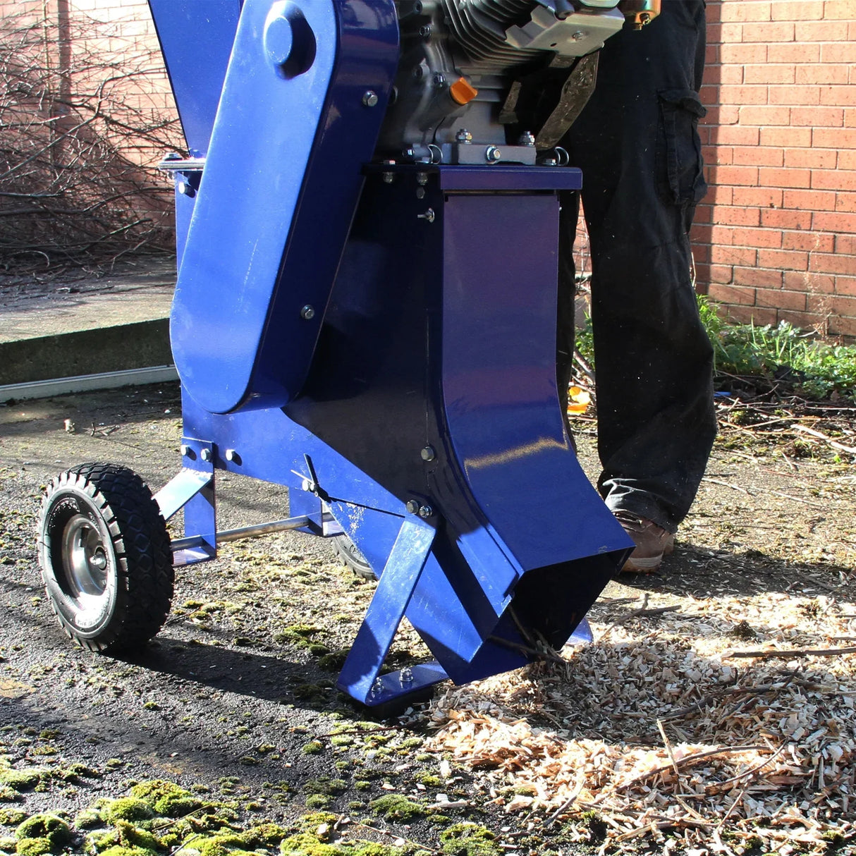 T-Mech 15HP wood chipper with a blue metal body, large chute, and sturdy wheels, shredding wood into fine chips on a gravel surface