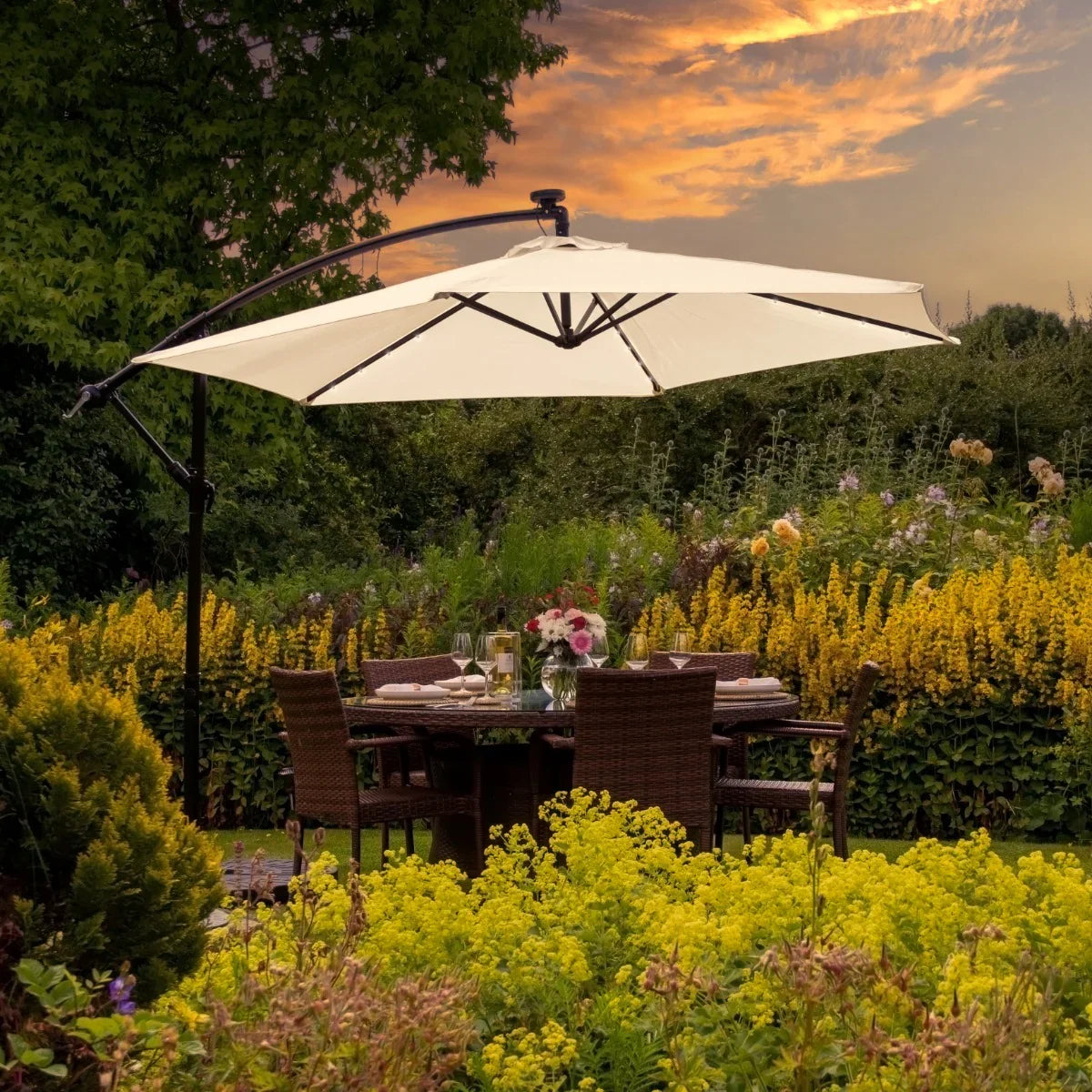 Cream 3m LED cantilever parasol with a sturdy black base, elegantly shading a garden dining area surrounded by vibrant flowers