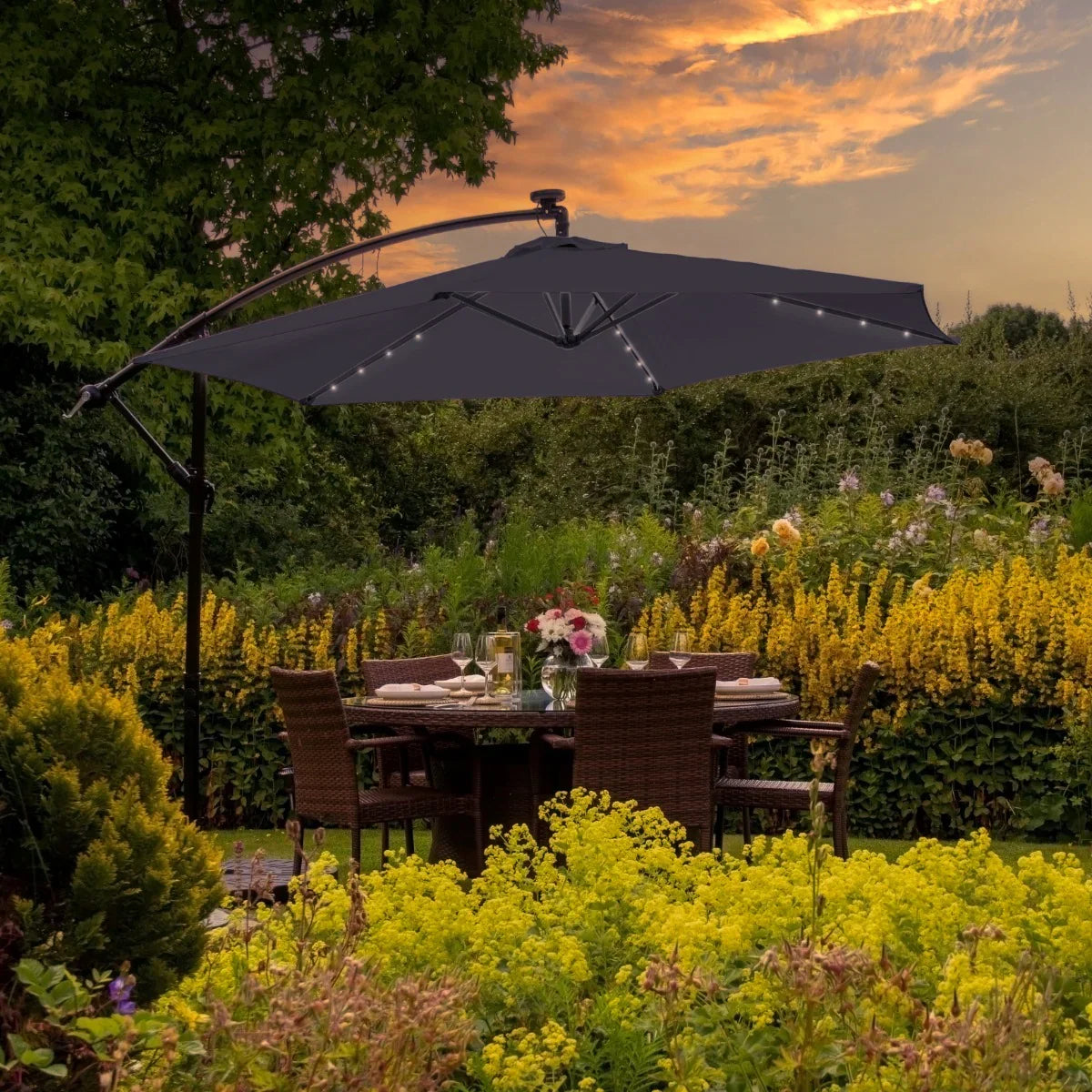 Grey 3m LED cantilever parasol with a sleek design, illuminated by soft lights, shading a stylish outdoor dining area surrounded by vibrant flowers