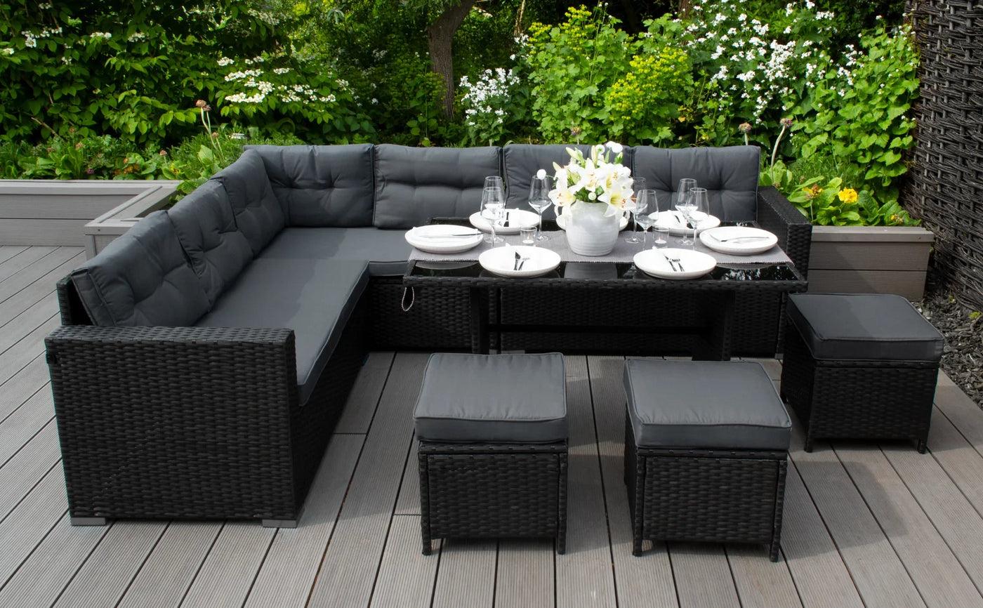 Stylish outdoor sectional sofa in black wicker with gray cushions, surrounded by greenery, featuring a dining table set with white flowers