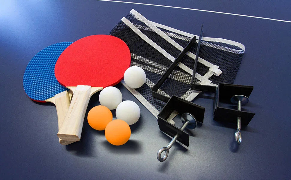 Red and blue table tennis paddles, white and orange balls, a net, and clamps arranged on a blue table surface
