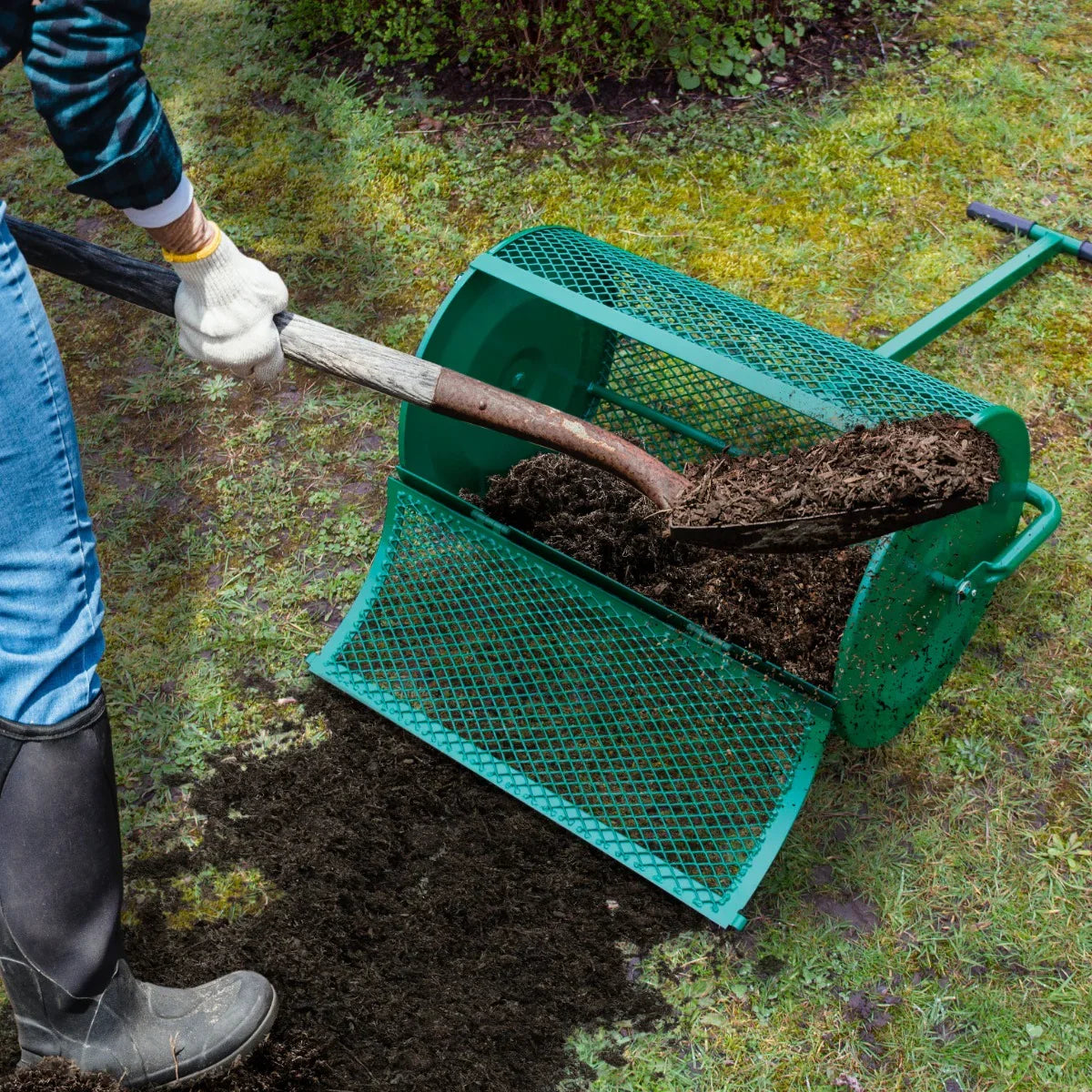 Green compost and peat moss spreader in use, featuring a mesh design and a shovel pouring dark compost onto the lawn