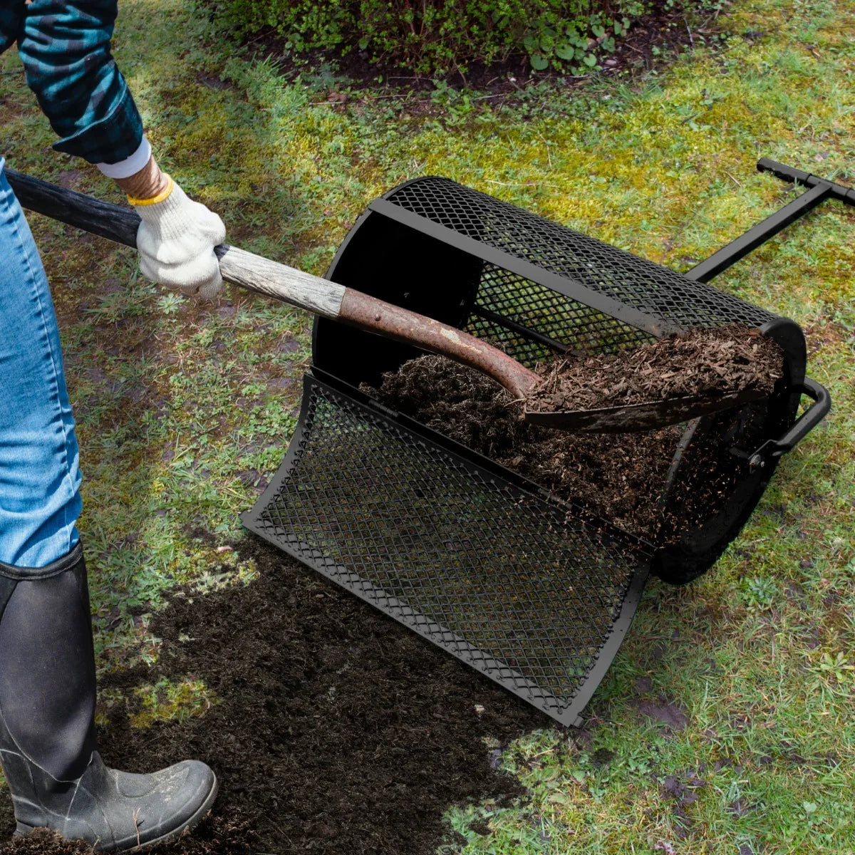 Black compost and peat moss spreader with a mesh design, being used to evenly distribute rich soil over a grassy area
