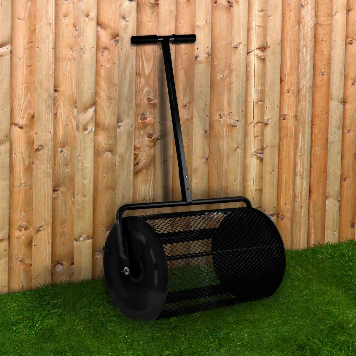 Black compost and peat moss spreader with a sturdy handle and mesh drum, set against a wooden fence and green grass background