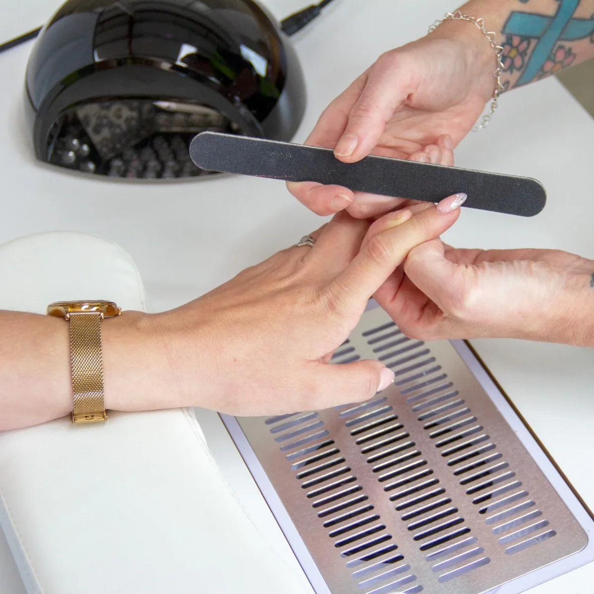 Professional manicure table with a sleek white surface, featuring a hand being manicured, a nail file, and a black UV lamp in the background