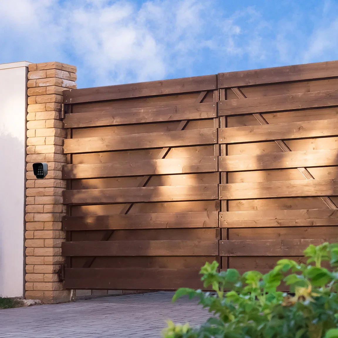 Wooden swing gate with horizontal slats, complemented by a stone pillar and wireless keypad, set against a blue sky backdrop