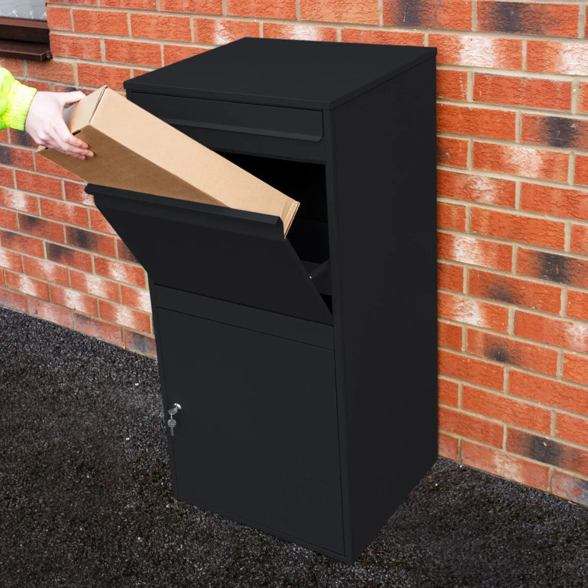 Black anti-theft parcel post box XL with a top slot for packages and a secure lower compartment, placed against a brick wall