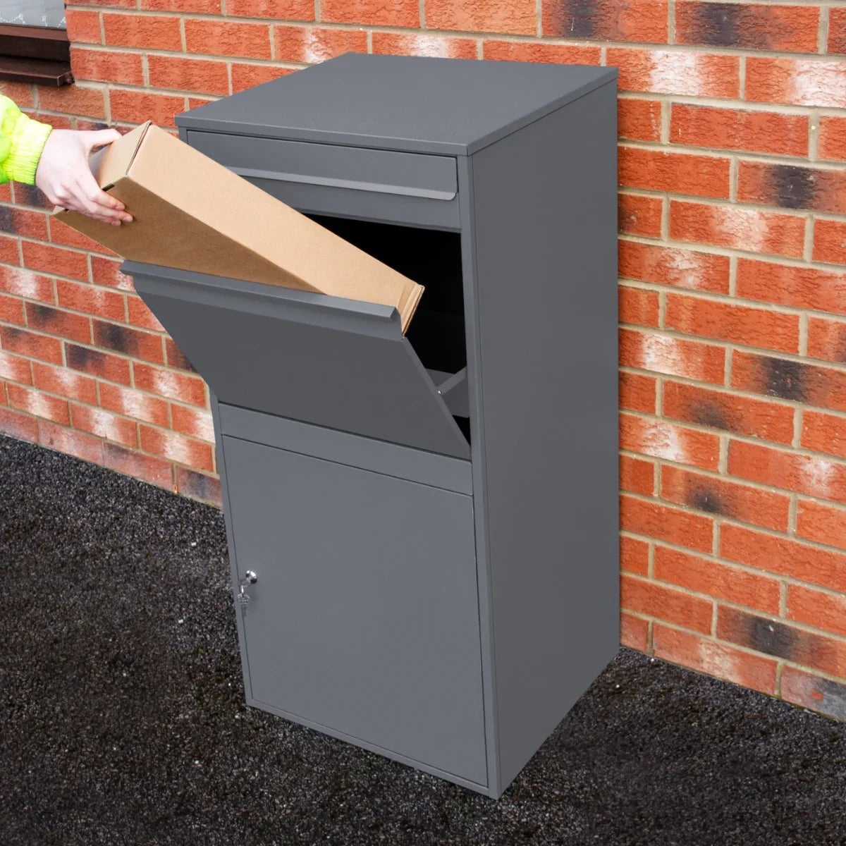 Grey anti-theft parcel post box XL with a top slot for packages and a secure lower compartment, set against a brick wall