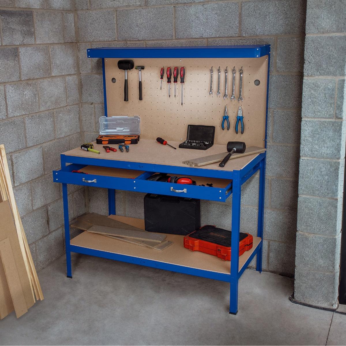 Blue workbench with pegboard, two drawers, tools hanging, and workspace for projects, set against a concrete wall