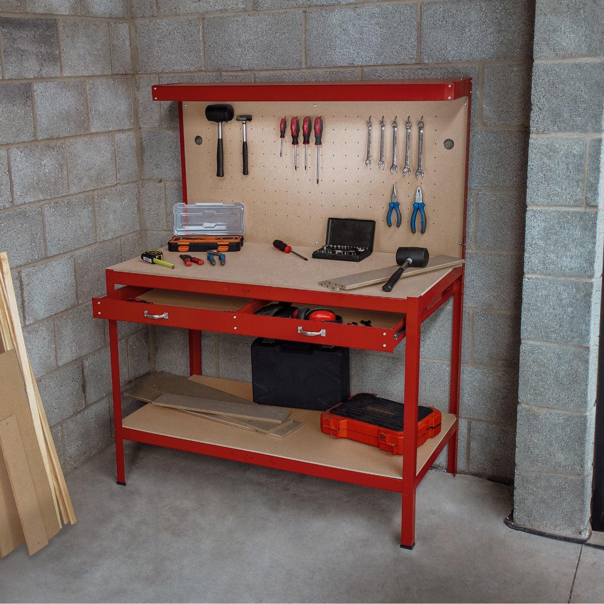 Red workbench with pegboard, drawer, and overhead light, featuring tools and storage, set against a concrete wall backdrop
