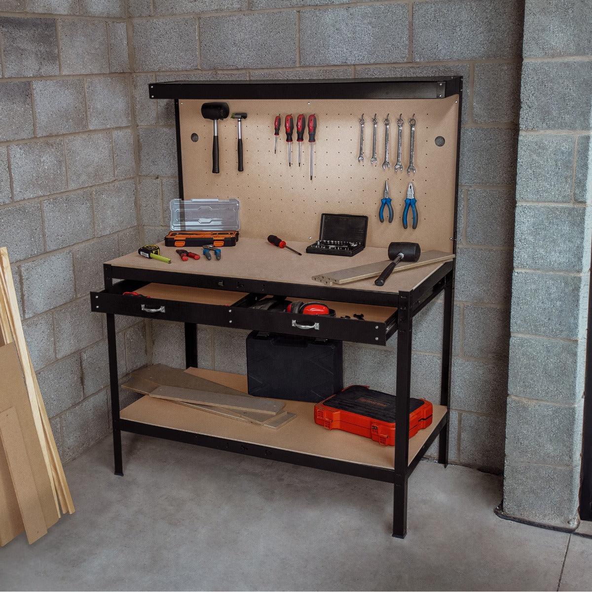 Black workbench featuring a pegboard with tools, two drawers, and an overhead light, set against a concrete wall