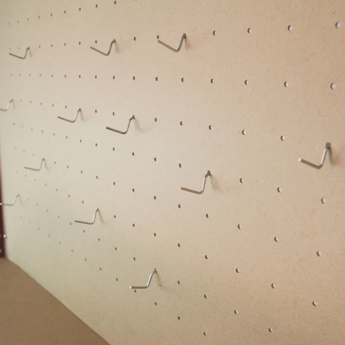 Close-up of a pegboard with multiple metal hooks, featuring a smooth beige surface and evenly spaced holes for tool organization