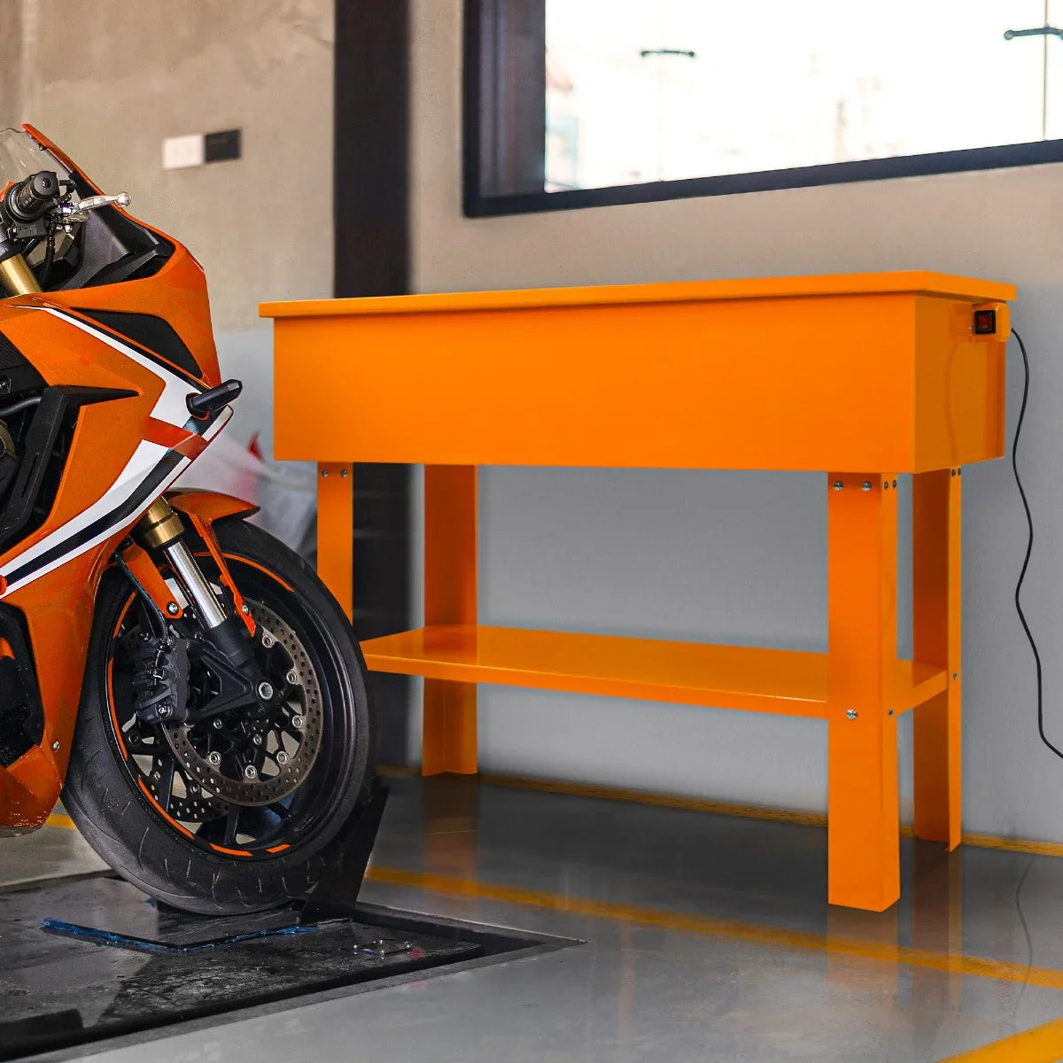 Bright orange 40-gallon parts washer with a sturdy design, featuring a lower shelf, positioned next to a motorcycle in a workshop setting