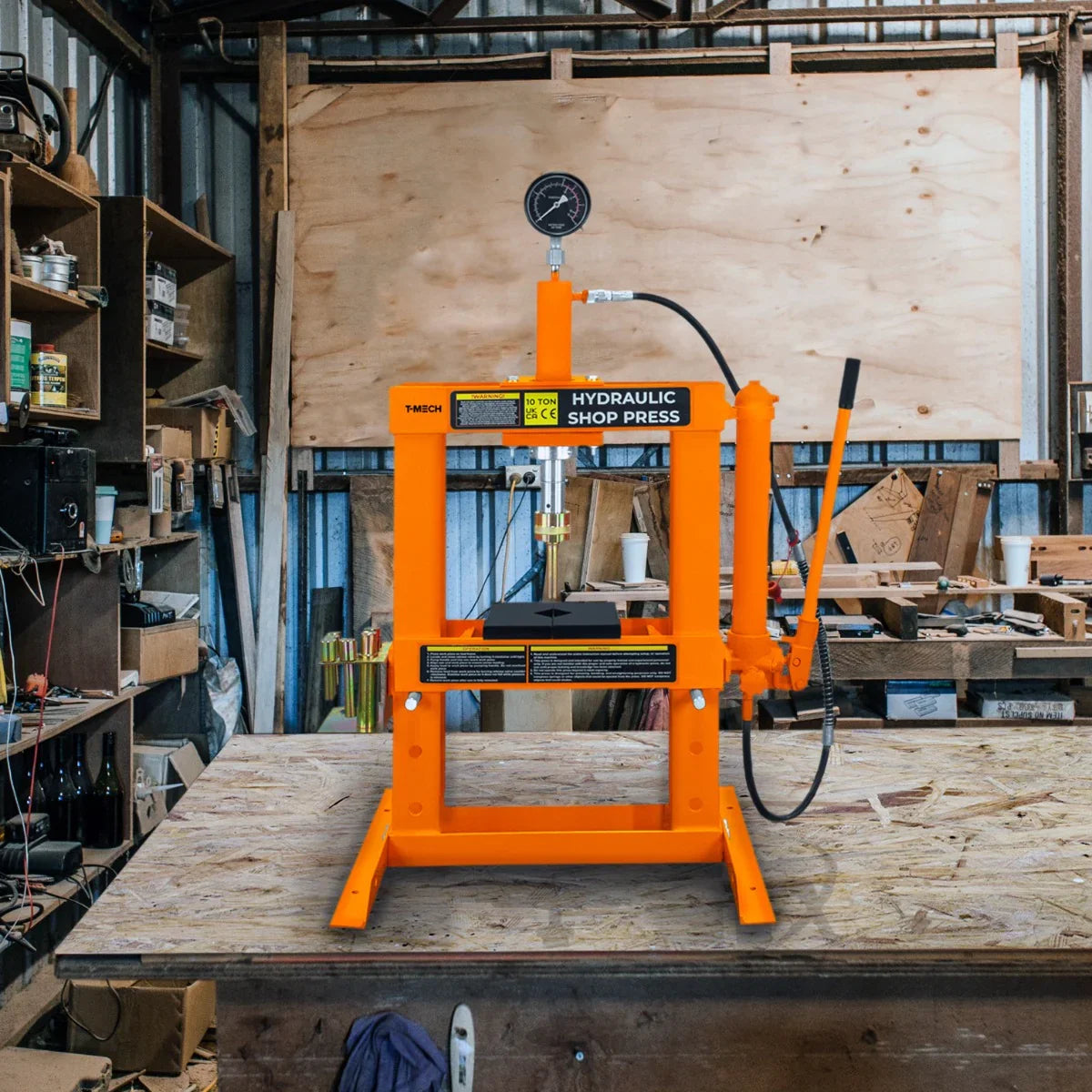 Bright orange hydraulic shop press with gauge, featuring a sturdy frame and flat pressing surface, set in a workshop environment