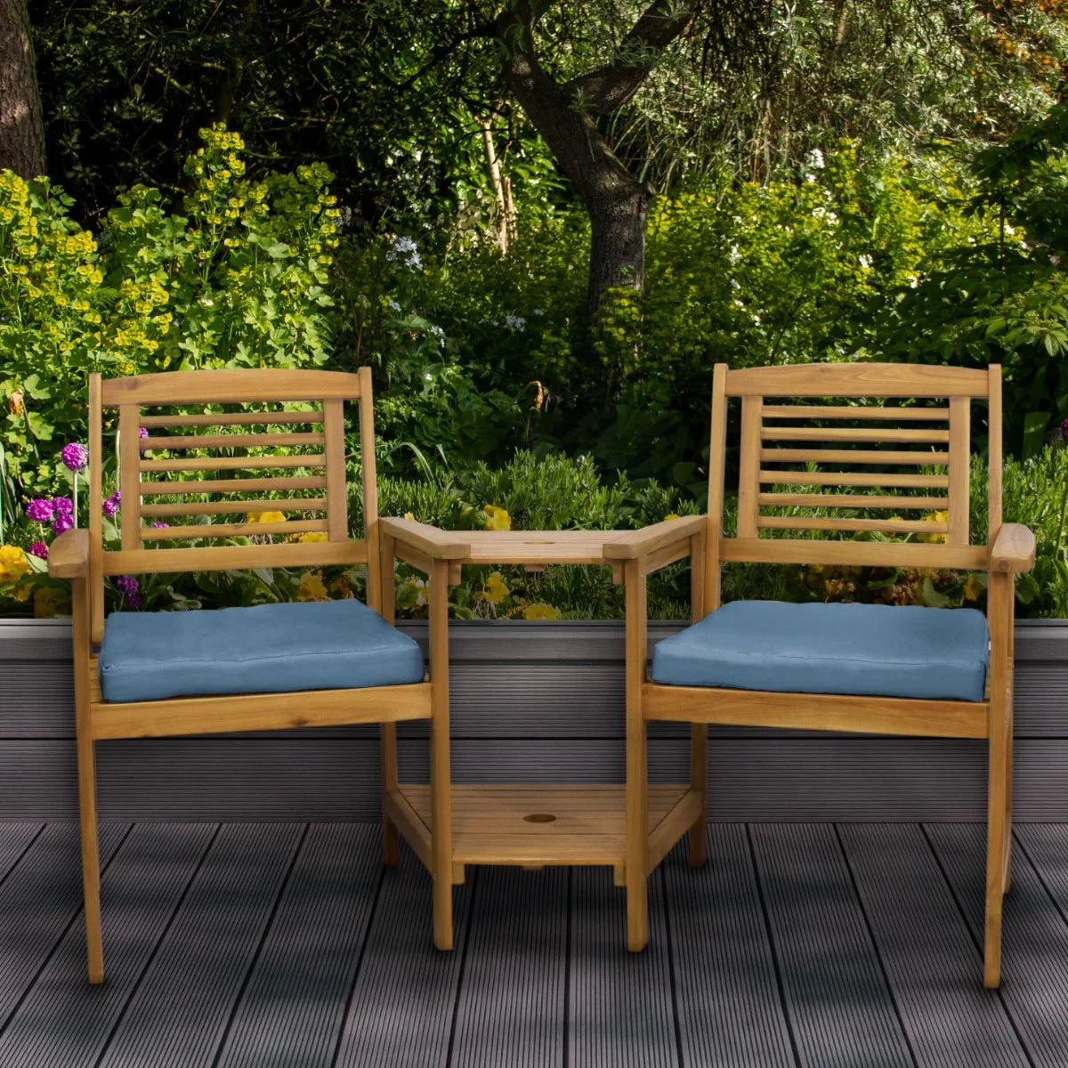 Natural wood companion seat with blue cushions, featuring slatted backs and a central table, set in a vibrant garden backdrop