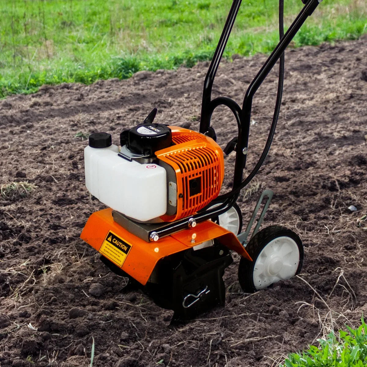 T-Mech petrol garden tiller with orange engine cover, black body, and white fuel tank, positioned on freshly tilled soil