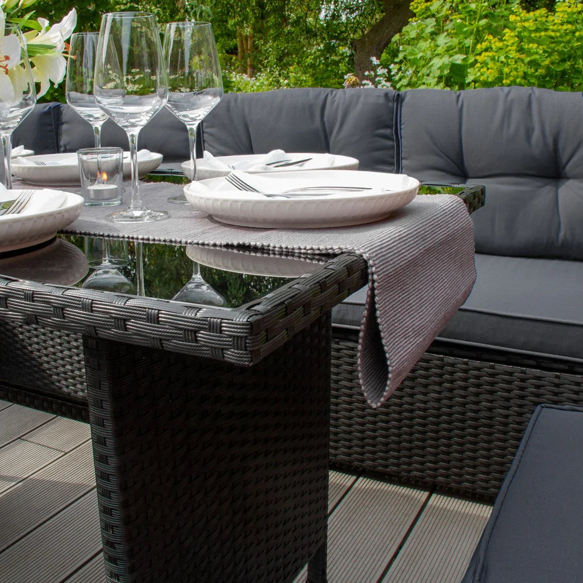 Black rattan corner set featuring plush gray cushions, a glass-top table, and elegant dinnerware, perfect for outdoor dining