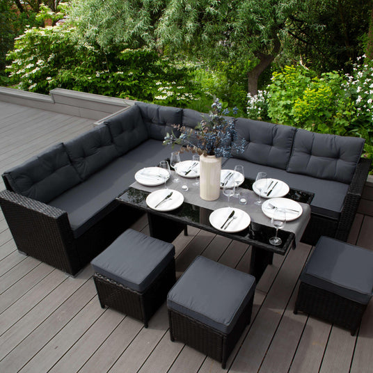 Stylish outdoor dining set featuring a dark wicker sectional sofa, sleek black table, and gray cushions, surrounded by greenery