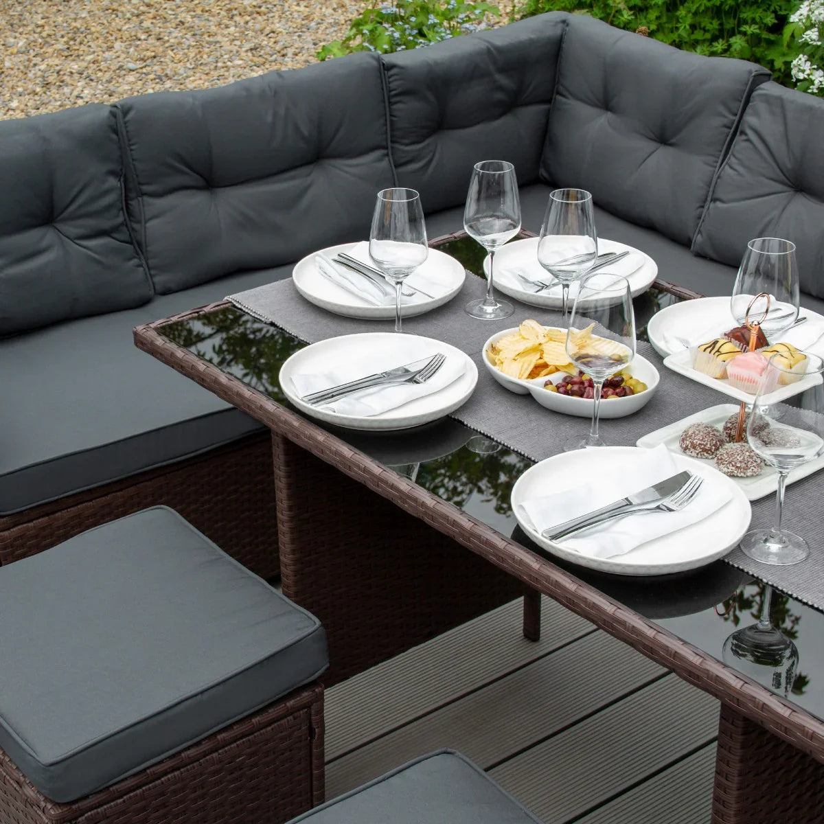 Brown rattan corner set featuring plush gray cushions, a glass tabletop, and an elegant dining setup with plates and glasses