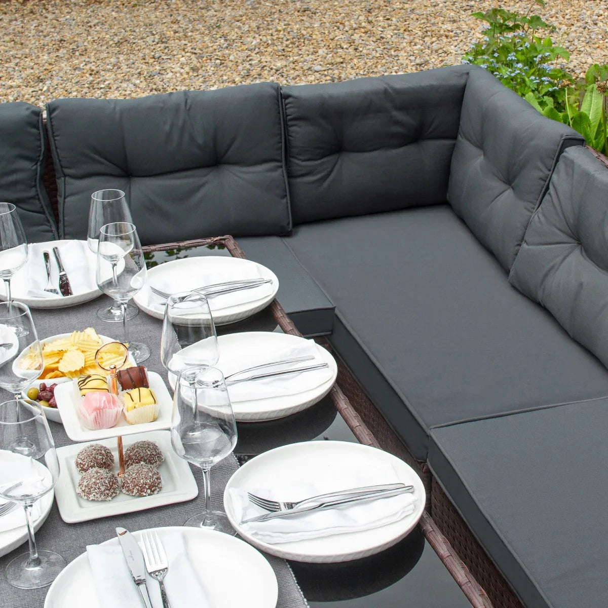 Brown rattan corner set with plush gray cushions, arranged around a dining table set with plates and elegant glassware
