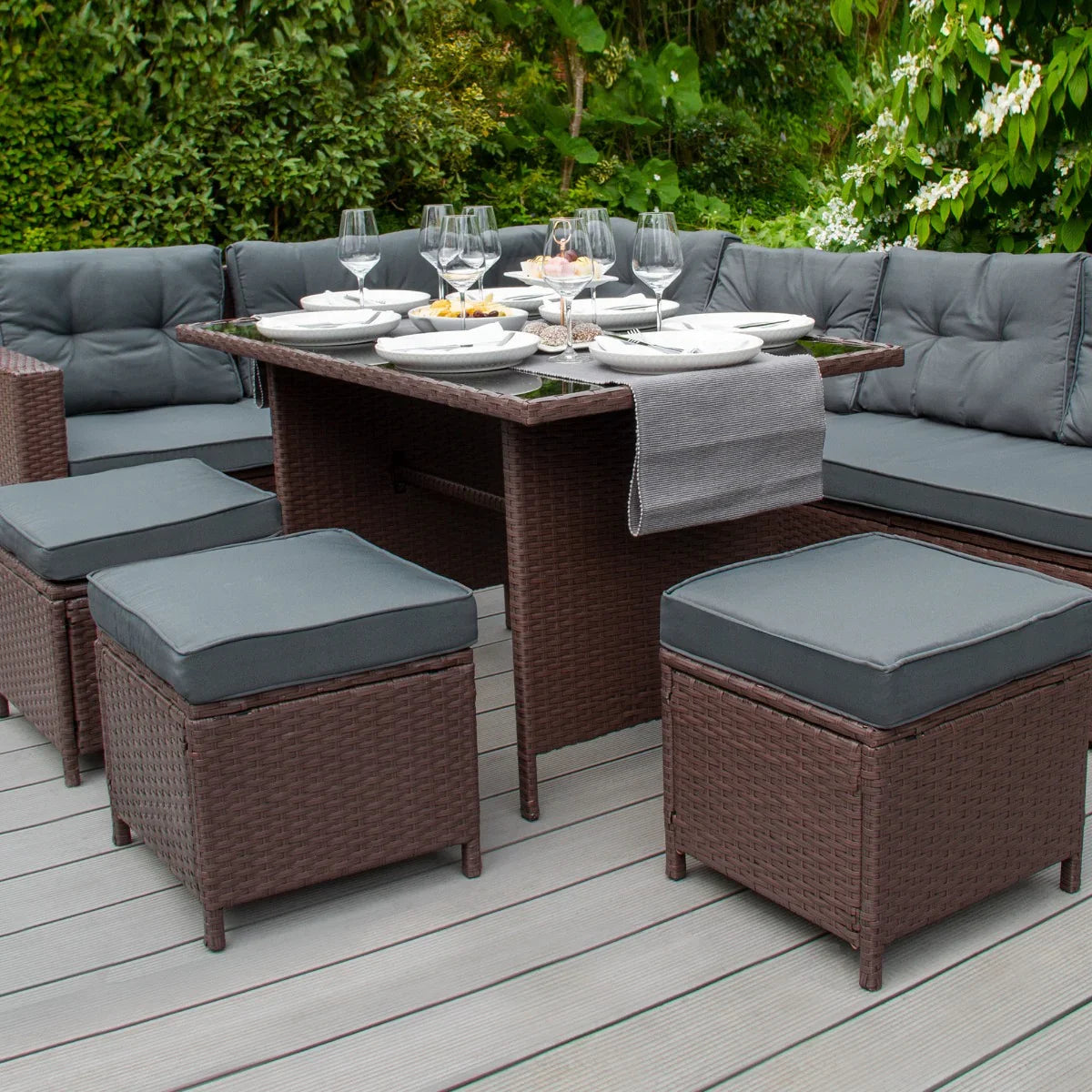 Brown rattan corner set featuring plush gray cushions, a glass-topped table, and stylish seating, perfect for outdoor dining