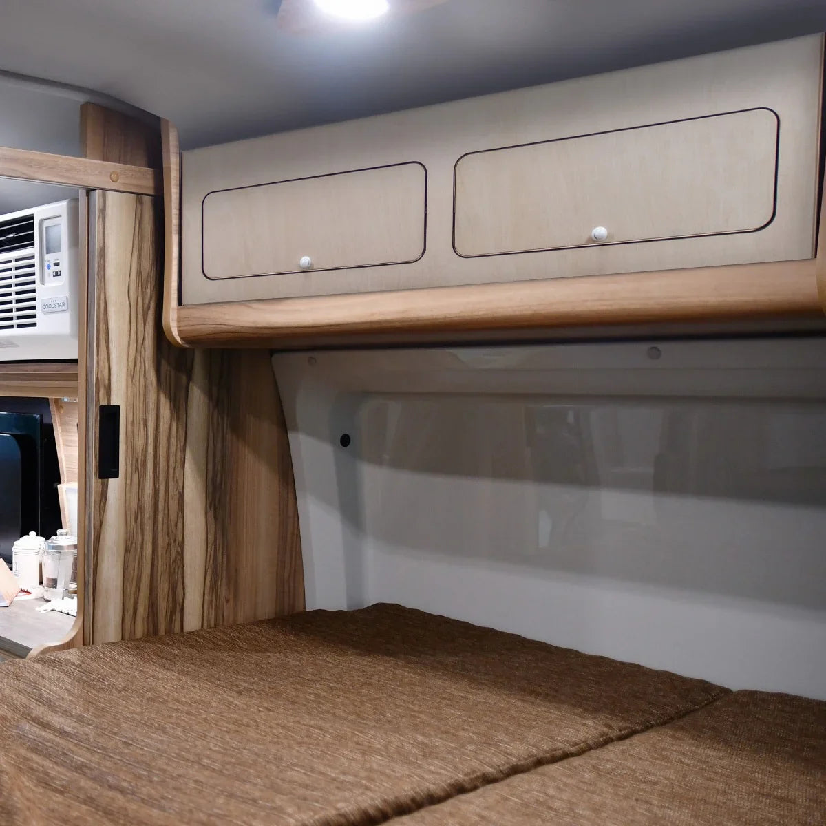 Overhead camper cabinet with black trim, featuring light wood finish, two drawers, and a sleek design, perfect for compact storage