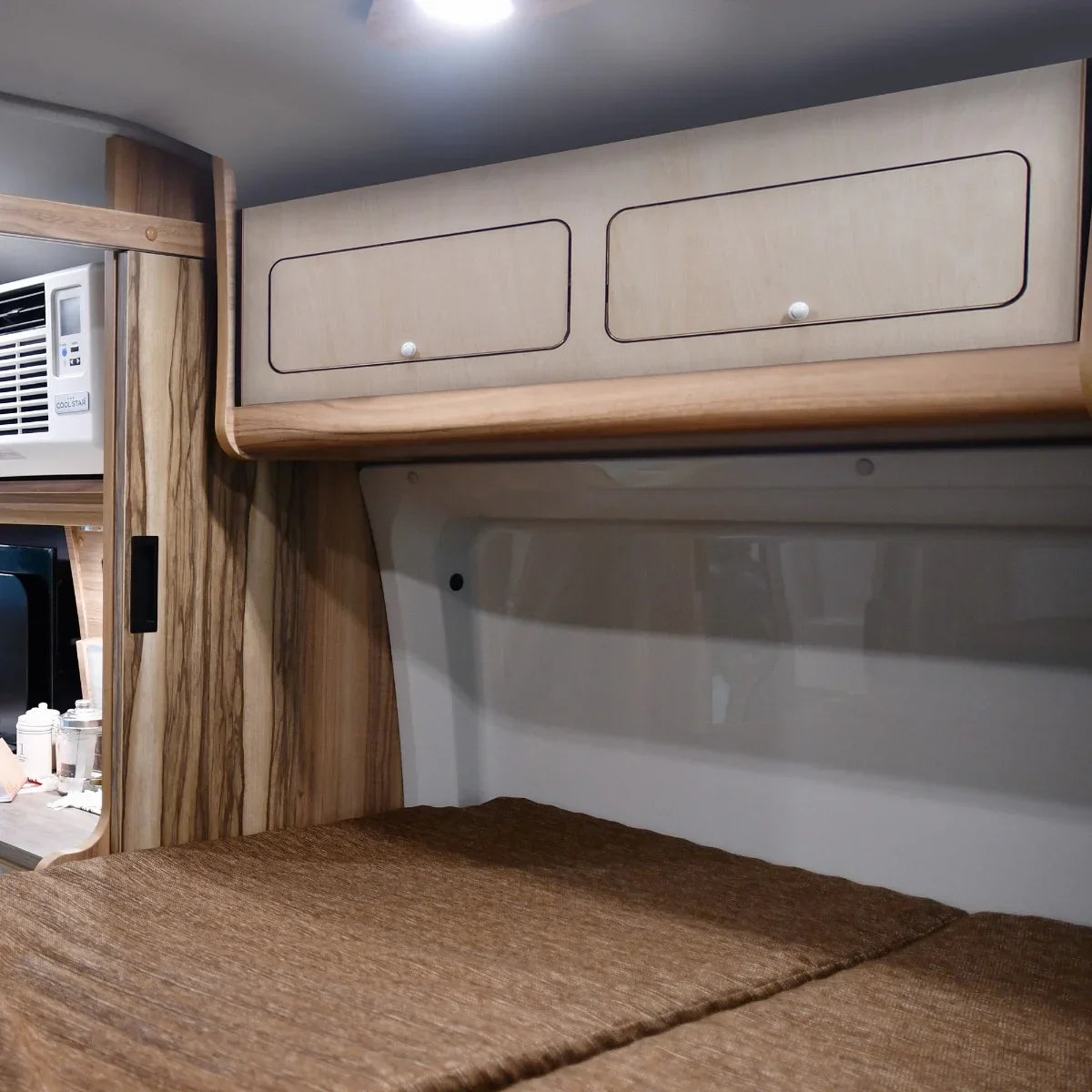 Overhead camper cabinet with black trim, featuring light wood finish, two drawers, and a sleek, modern design for efficient storage