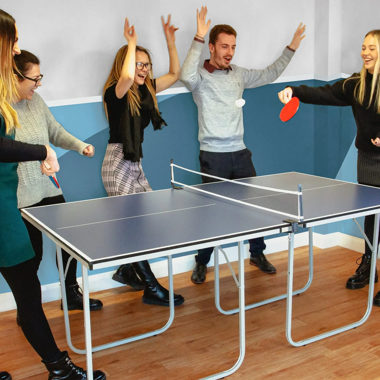 Folding table tennis table with blue surface, surrounded by four people enjoying a game, showcasing paddles and balls in action
