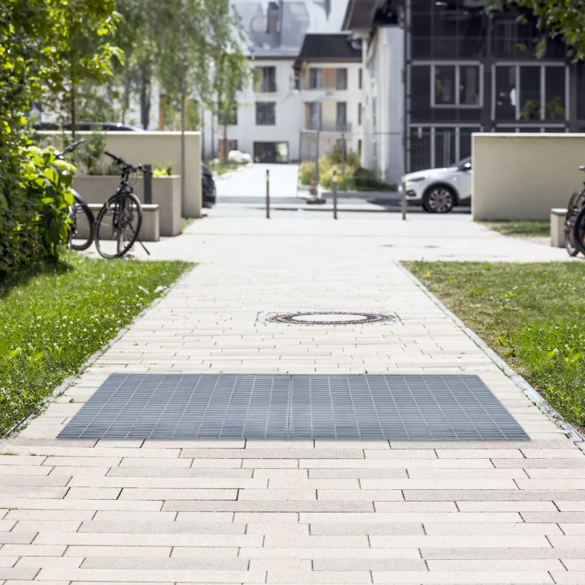Galvanised grating measuring 1000mm x 600mm, featuring a durable, textured surface, set on a paved pathway in a landscaped area