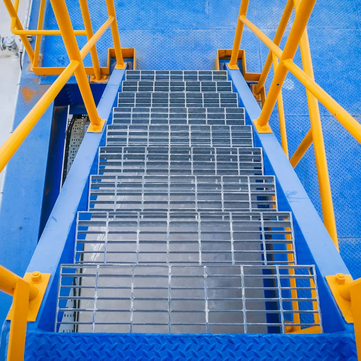 Galvanised grating stairway with a sturdy metal surface, featuring a grid pattern, surrounded by bright yellow safety railings