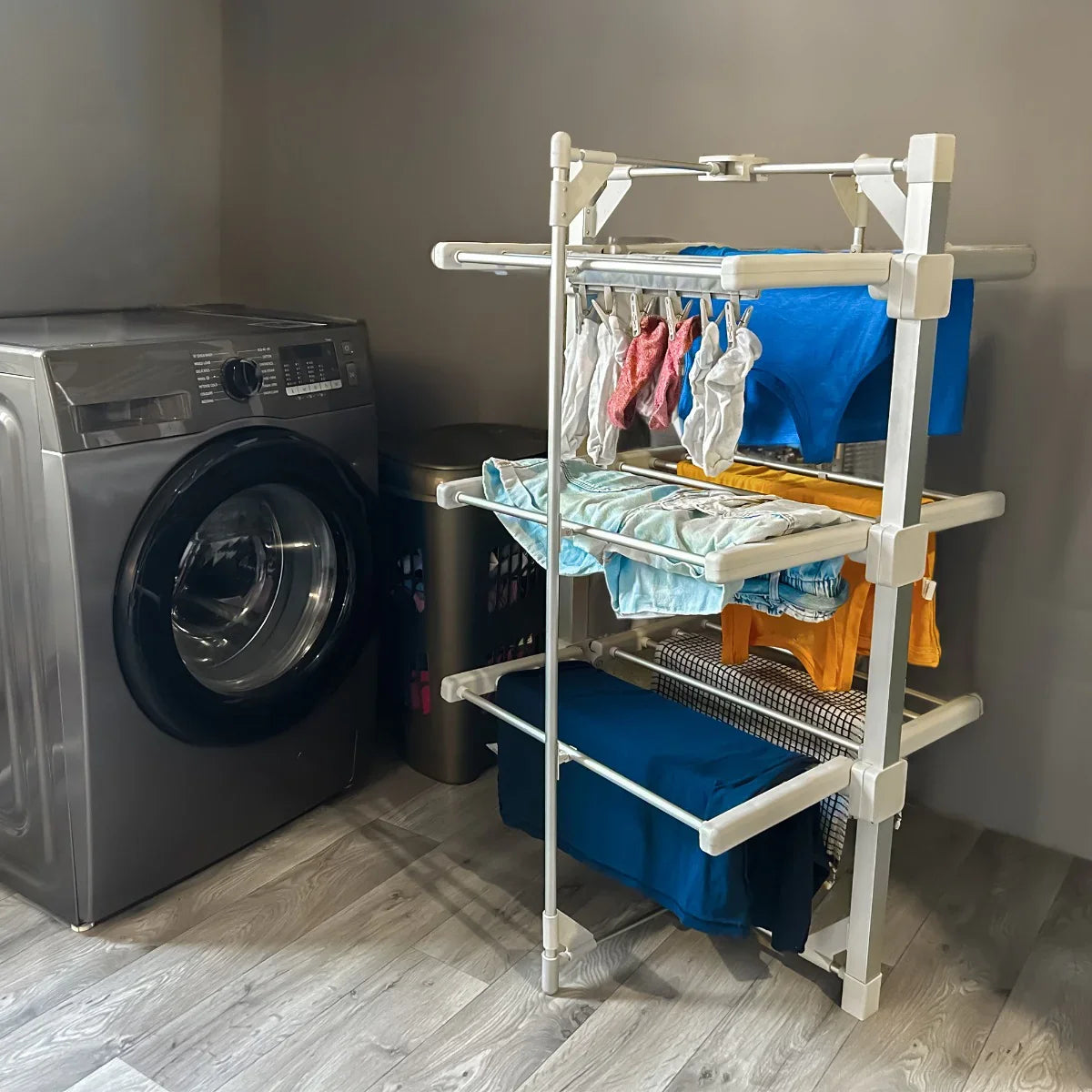 Heated clothes airer with multiple tiers, featuring colorful garments drying, set beside a modern washing machine in a laundry room